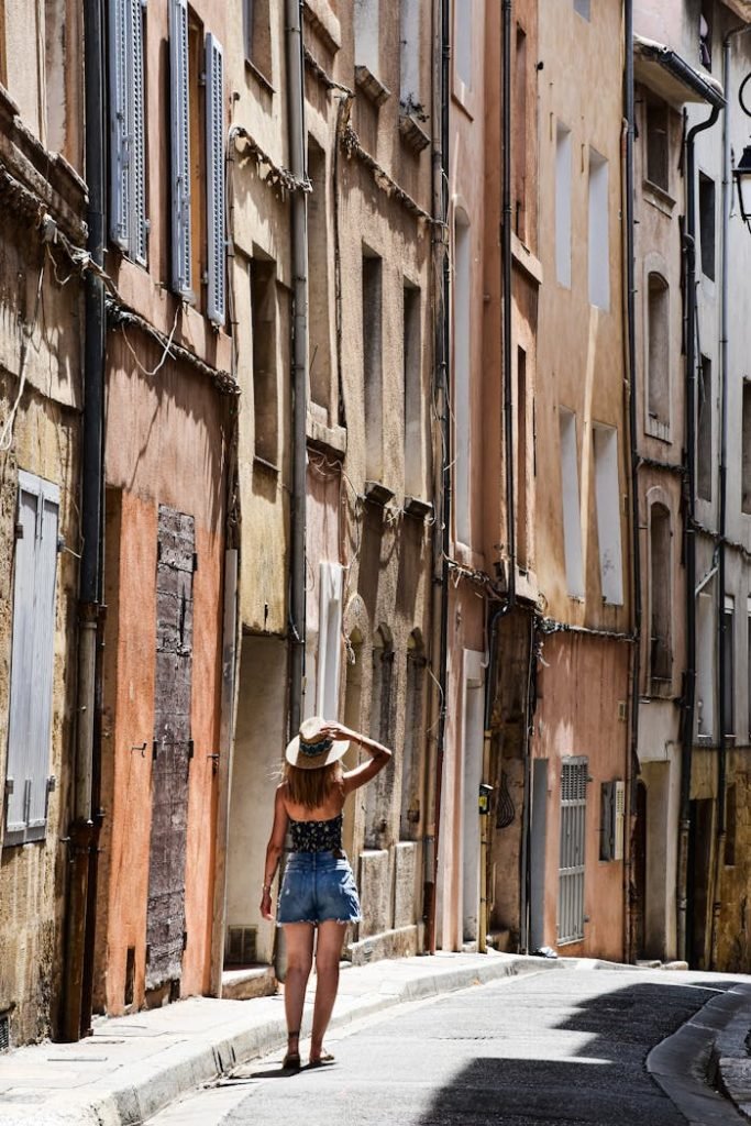 woman-walking-in-charming-aix-en-provence-street-29983877 A woman strolls through a picturesque narrow street in Aix-en-Provence, France, basking in the summer sun.